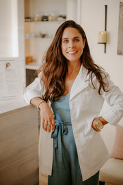 A smiling woman in a white coat stands indoors, arms crossed, embodying the nurturing and health-focused ethos of WeNatal's prenatal supplement range.